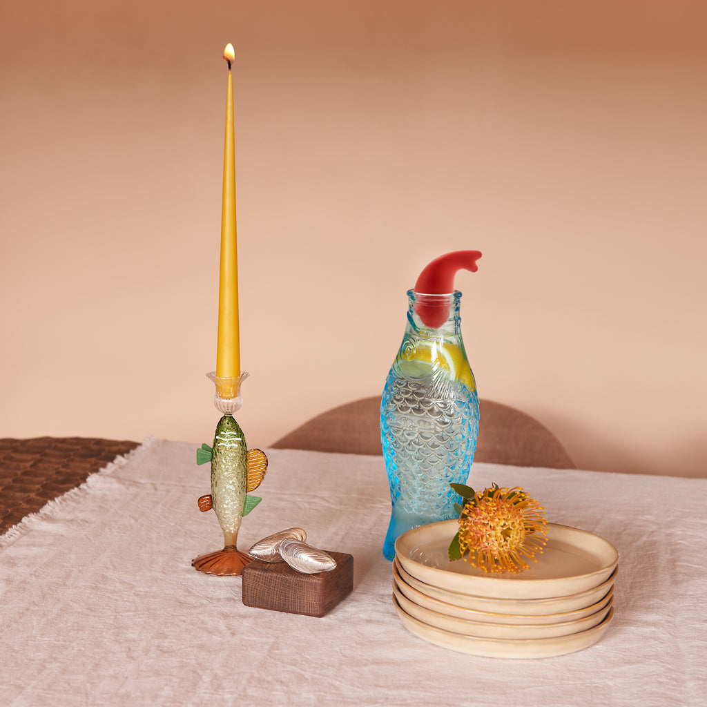 Geschenkbox Looks Fishy van Collections by Gaav Interieur: groene vis-kandelaar met gele taper kaars, lichtblauwe vis-karaf met rode stopper en zilver mosselbestek op een gedekte tafel