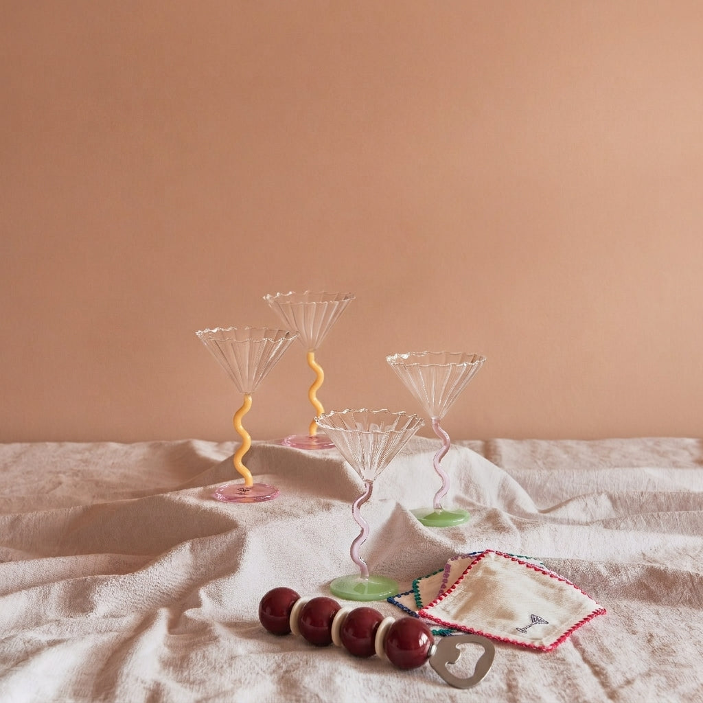 Inhoud van geschenkbox Social Gathering: vier &klevering Curve coupe cocktailglazen in caramel en roze, geborduurde Zigzag cocktailservetten en de Addison Ross Bobbin flesopener in Cherry & Cappuccino